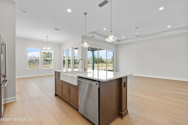 kitchen featuring sink, decorative light fixtures, a tray ceiling, dishwasher, and an island with sink