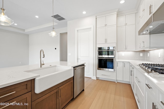 kitchen with appliances with stainless steel finishes, pendant lighting, sink, white cabinets, and light stone counters