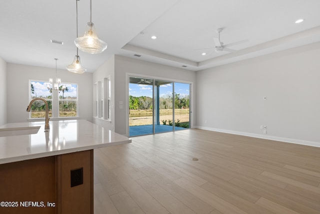 unfurnished living room with ceiling fan with notable chandelier, sink, a raised ceiling, and light hardwood / wood-style floors