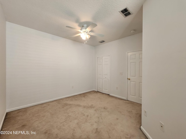 unfurnished bedroom featuring ceiling fan, light colored carpet, and a textured ceiling