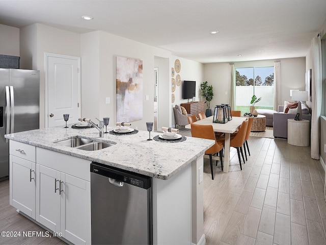 kitchen featuring sink, appliances with stainless steel finishes, a kitchen island with sink, white cabinetry, and light stone counters