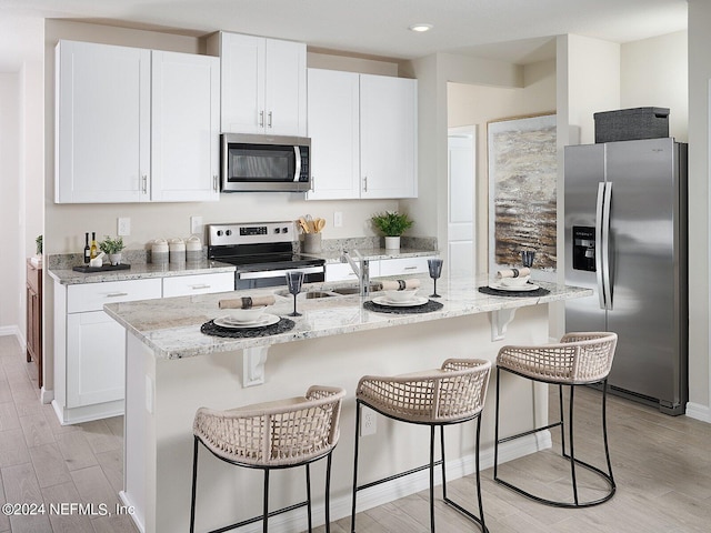 kitchen with appliances with stainless steel finishes, white cabinets, light hardwood / wood-style floors, and an island with sink