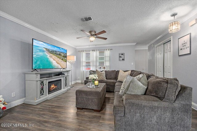 living room featuring dark wood-type flooring, a textured ceiling, ceiling fan, and ornamental molding