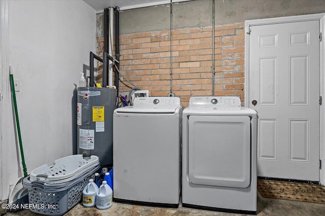 clothes washing area with brick wall, electric water heater, and washer and dryer