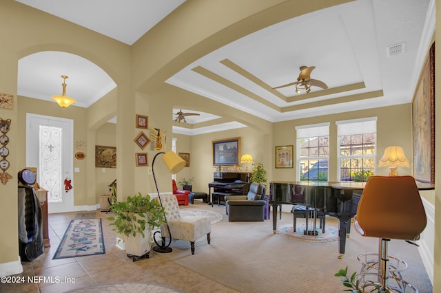 tiled living room with ornamental molding, ceiling fan, and a tray ceiling