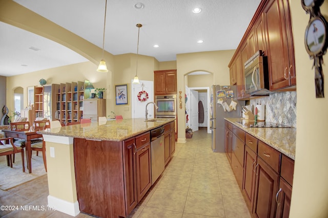 kitchen with hanging light fixtures, light stone countertops, appliances with stainless steel finishes, light tile patterned floors, and a kitchen island with sink