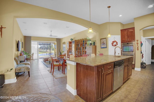 kitchen with decorative light fixtures, light tile patterned flooring, an island with sink, light stone countertops, and appliances with stainless steel finishes