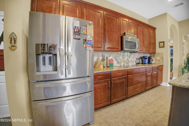 kitchen featuring appliances with stainless steel finishes, light tile patterned flooring, decorative backsplash, and light stone counters