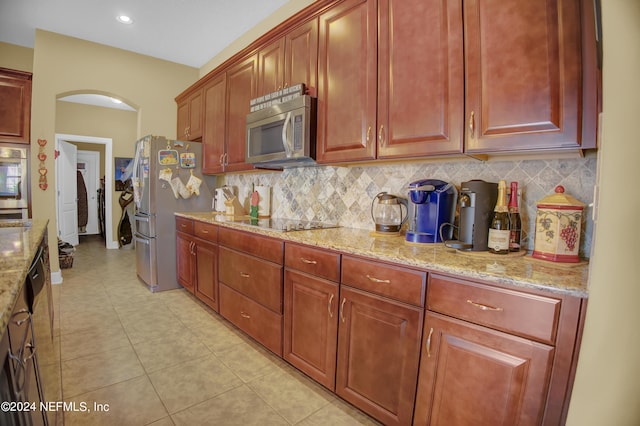 kitchen with appliances with stainless steel finishes, light tile patterned flooring, light stone countertops, and backsplash