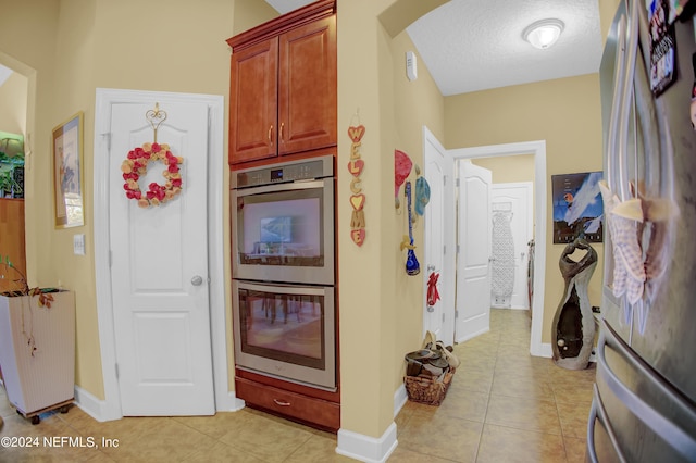 kitchen with appliances with stainless steel finishes, light tile patterned flooring, and a textured ceiling