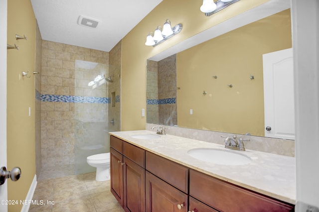 bathroom with tile patterned flooring, a tile shower, toilet, and double sink vanity