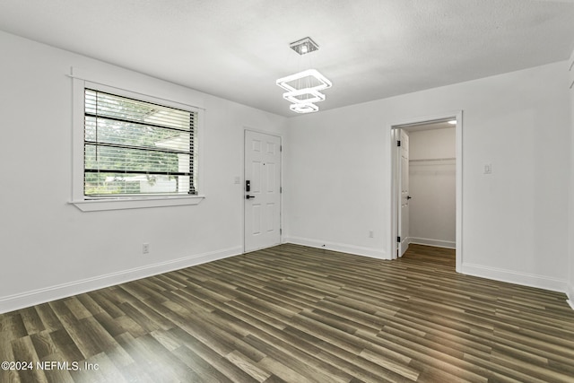 spare room with dark wood-type flooring, an inviting chandelier, and a textured ceiling