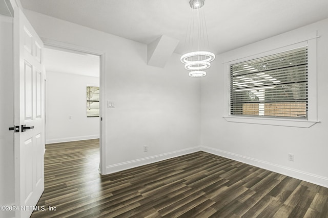 spare room featuring dark wood-type flooring and a notable chandelier