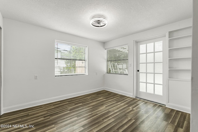 empty room featuring dark wood-type flooring, built in features, and a textured ceiling