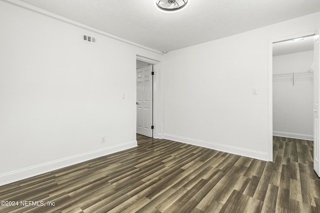 unfurnished bedroom featuring a spacious closet, dark hardwood / wood-style flooring, a closet, and a textured ceiling