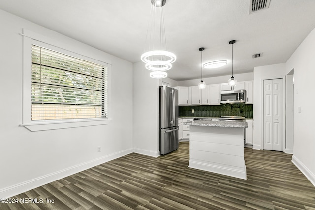 kitchen featuring pendant lighting, stainless steel appliances, white cabinets, a kitchen island, and decorative backsplash