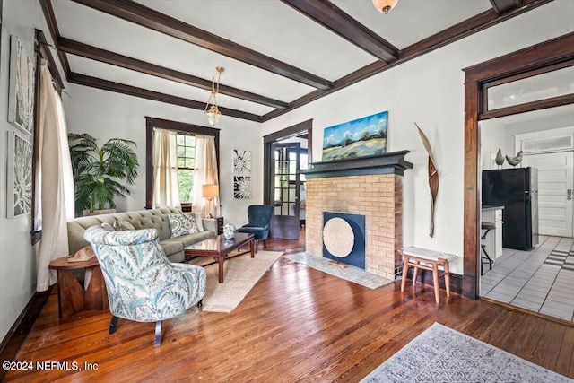 living area featuring a brick fireplace, baseboards, beamed ceiling, and hardwood / wood-style floors