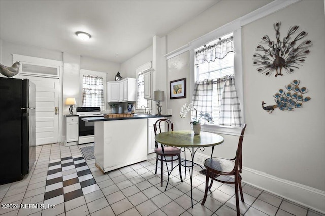 kitchen featuring white range with electric stovetop, dark countertops, freestanding refrigerator, a peninsula, and a sink