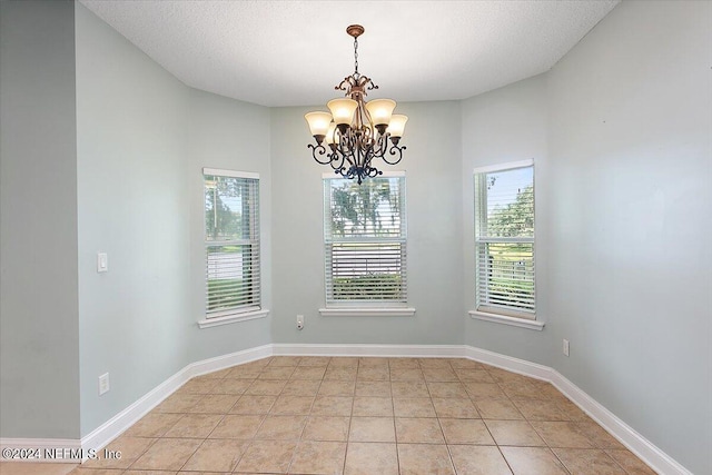 tiled spare room featuring an inviting chandelier and a textured ceiling