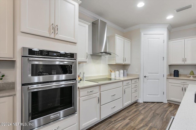 kitchen featuring stainless steel double oven, wall chimney exhaust hood, dark wood-type flooring, white cabinetry, and crown molding