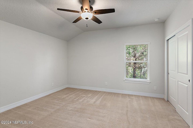 carpeted empty room featuring vaulted ceiling, ceiling fan, and a textured ceiling