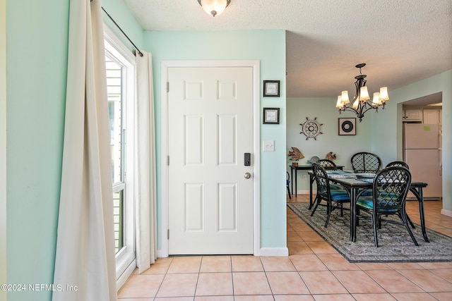 entryway with light tile patterned flooring, an inviting chandelier, and a textured ceiling