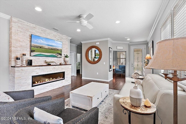 living room featuring ornamental molding, a fireplace, a textured ceiling, dark wood-type flooring, and ceiling fan