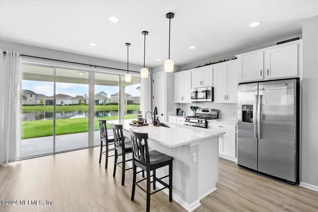 kitchen featuring appliances with stainless steel finishes, light hardwood / wood-style flooring, white cabinets, a water view, and a kitchen island with sink