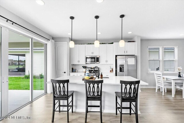 kitchen with appliances with stainless steel finishes, tasteful backsplash, pendant lighting, light wood-type flooring, and an island with sink