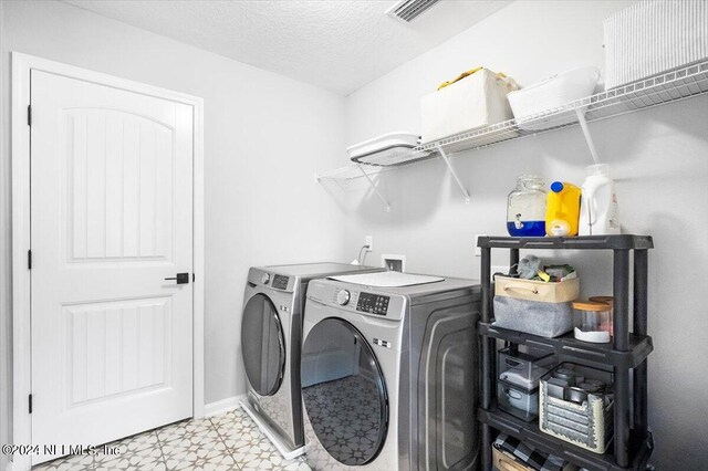 clothes washing area with a textured ceiling, washer and dryer, and light tile patterned floors