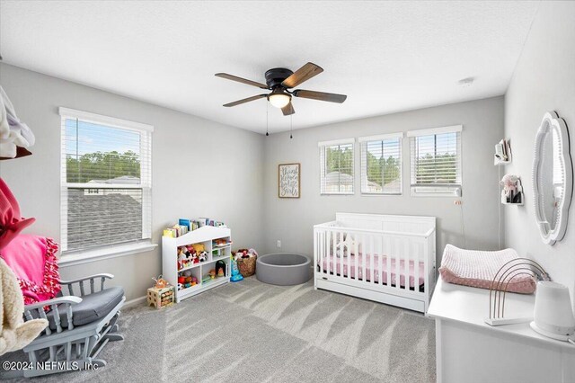 carpeted bedroom featuring multiple windows, a nursery area, and ceiling fan