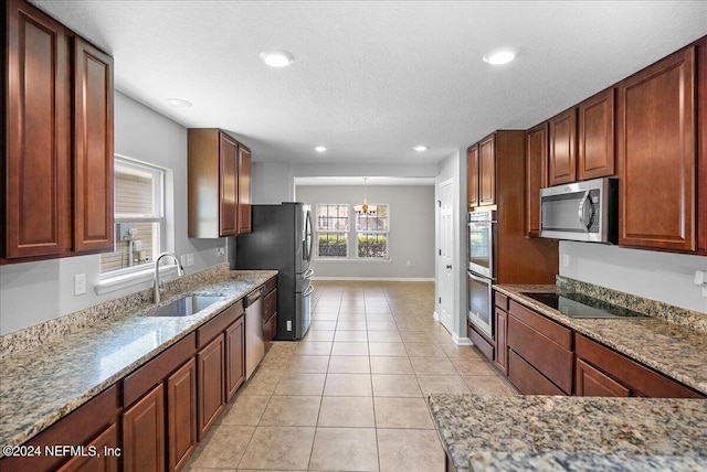 kitchen with light tile patterned floors, appliances with stainless steel finishes, a notable chandelier, light stone counters, and sink