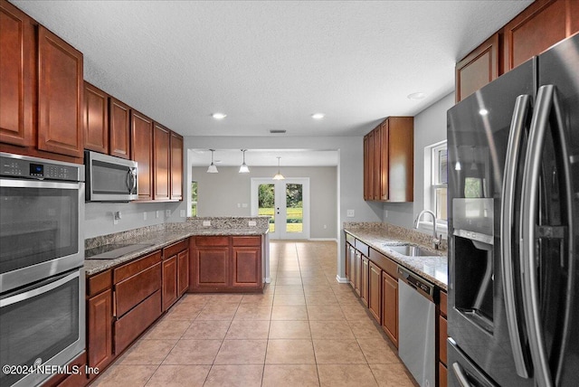 kitchen with decorative light fixtures, black appliances, kitchen peninsula, sink, and light stone countertops