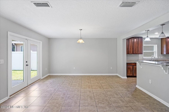 kitchen with light tile patterned floors, french doors, light stone countertops, and pendant lighting