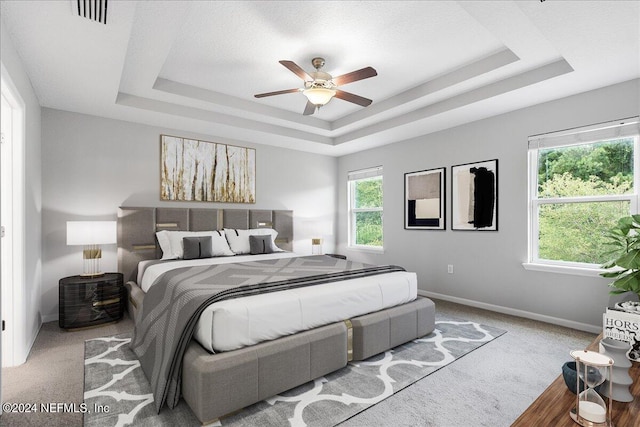 carpeted bedroom featuring ceiling fan and a tray ceiling