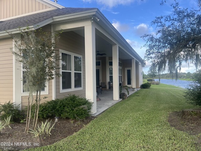 view of property exterior featuring a water view, a lawn, ceiling fan, and a patio