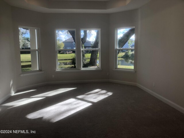 unfurnished room with a tray ceiling and dark colored carpet