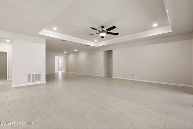 tiled empty room with a raised ceiling, ornamental molding, and ceiling fan