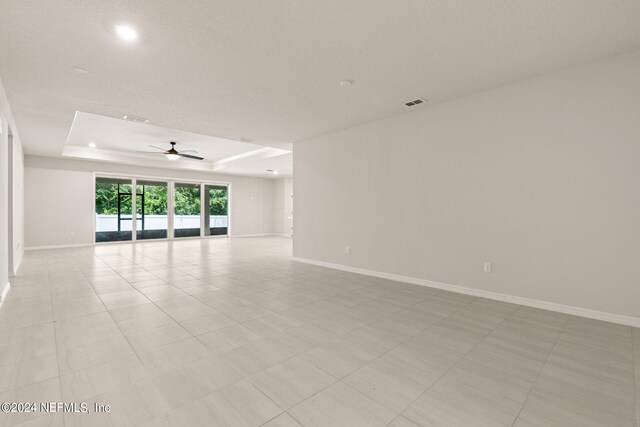 empty room with a raised ceiling, light tile patterned flooring, and ceiling fan