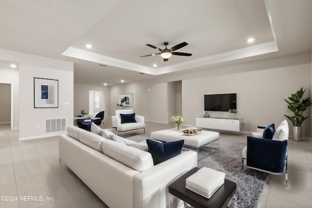 living room with light tile patterned floors, a tray ceiling, ornamental molding, and ceiling fan