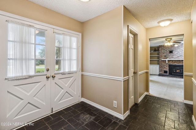 doorway to outside with ceiling fan, a textured ceiling, and a brick fireplace