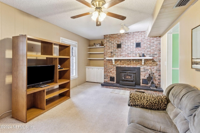 living room featuring a wood stove, light carpet, ceiling fan, and a textured ceiling