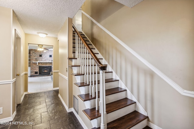 stairs featuring ceiling fan, a fireplace, and a textured ceiling