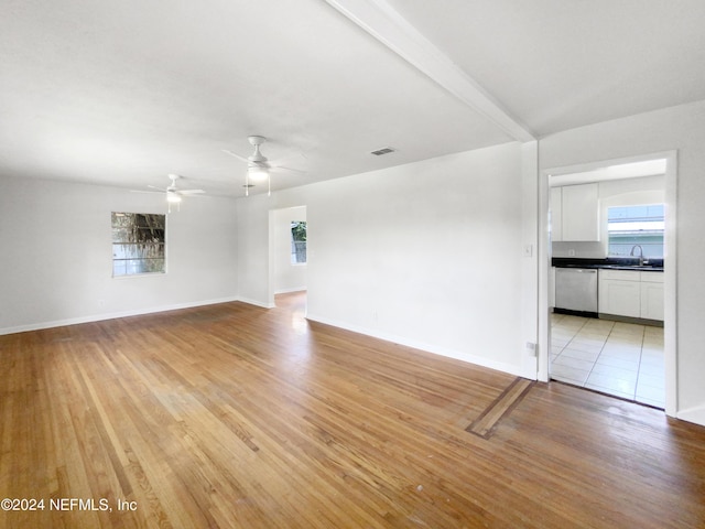 unfurnished living room featuring ceiling fan, sink, light hardwood / wood-style flooring, and beam ceiling