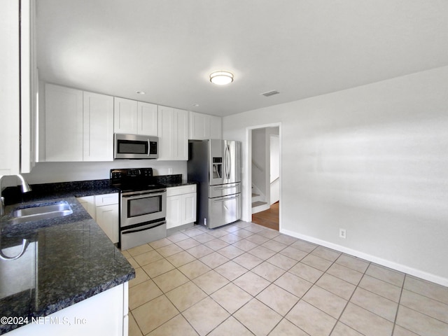 kitchen with white cabinetry, sink, dark stone countertops, stainless steel appliances, and light tile patterned flooring