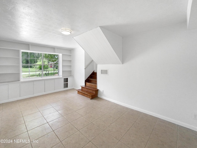 unfurnished living room featuring built in shelves, light tile patterned floors, and a textured ceiling