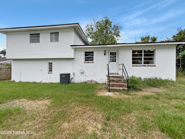 rear view of property with central air condition unit and a yard