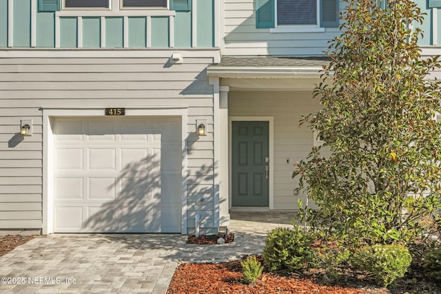 view of exterior entry with driveway, a garage, and roof with shingles