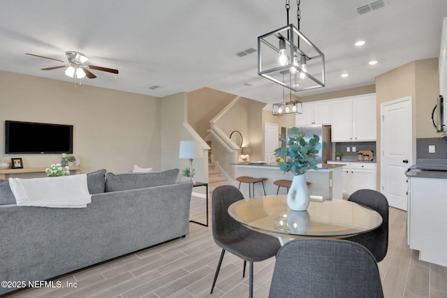 dining space featuring stairs, a ceiling fan, visible vents, and wood tiled floor