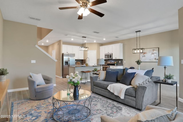 living room featuring visible vents, baseboards, light wood-style floors, and ceiling fan with notable chandelier